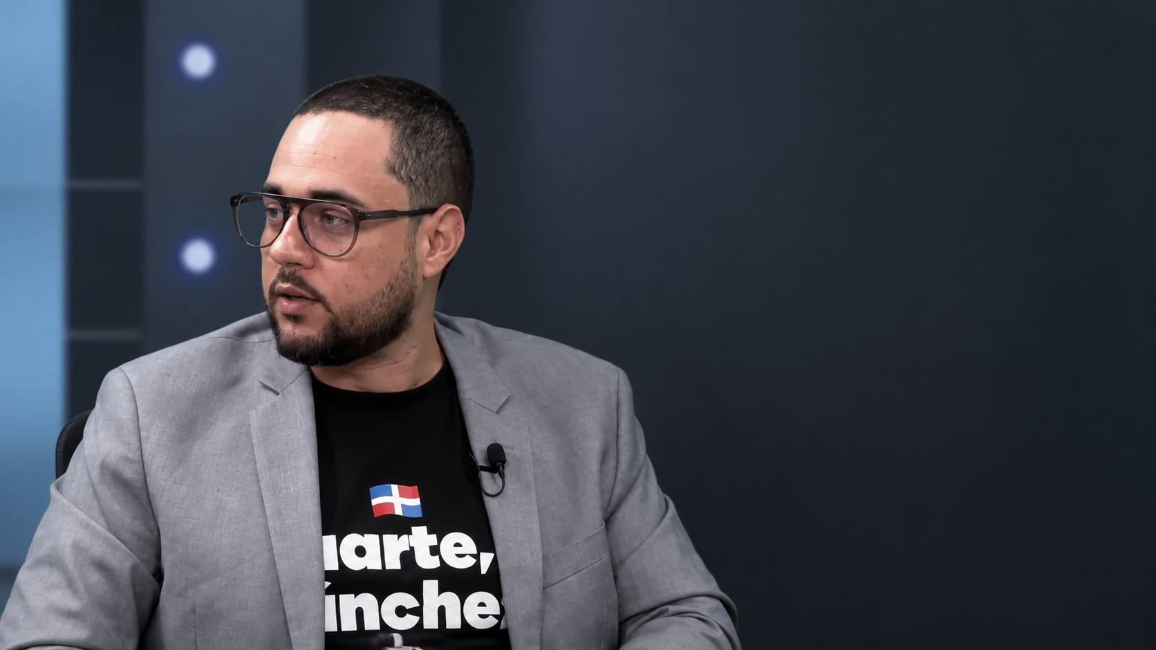 Pedro Vital durante una entrevista, con chaqueta gris y camiseta con la bandera dominicana